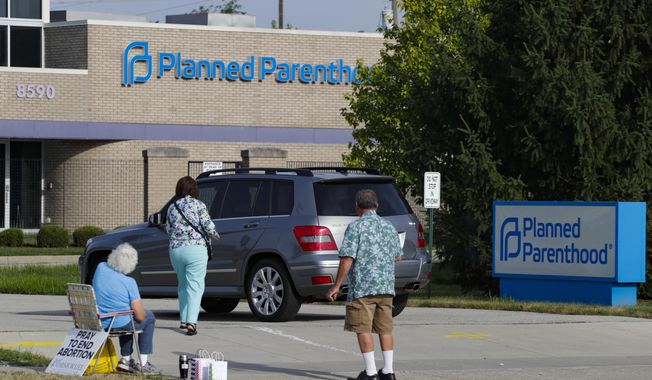 Abortion protesters attempt to handout literature as they stand in the driveway of a Planned Parenthood clinic in Indianapolis, Aug. 16, 2019. The number of abortions being performed in Indiana has dropped steeply ahead of a court ruling that has a Republican-backed abortion ban set to potentially take effect in the coming weeks. (AP Photo/Michael Conroy, File)
