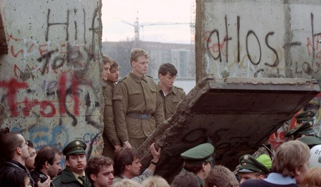 ** PACKAGE TO GO WITH THE 20TH ANNIVERSARY OF THE FALL OF THE BERLIN WALL ** SIX OF TWENTY ** FILE - East German border guards look through a hole in the Berlin wall after demonstrators pulled down one segment of the wall at Brandenburg gate in this Nov. 11, 1989 file picture. Monday, Nov. 9, 2009 marks the 20th anniversary of the fall of the Berlin Wall. (AP Photo/Lionel Cironneau)