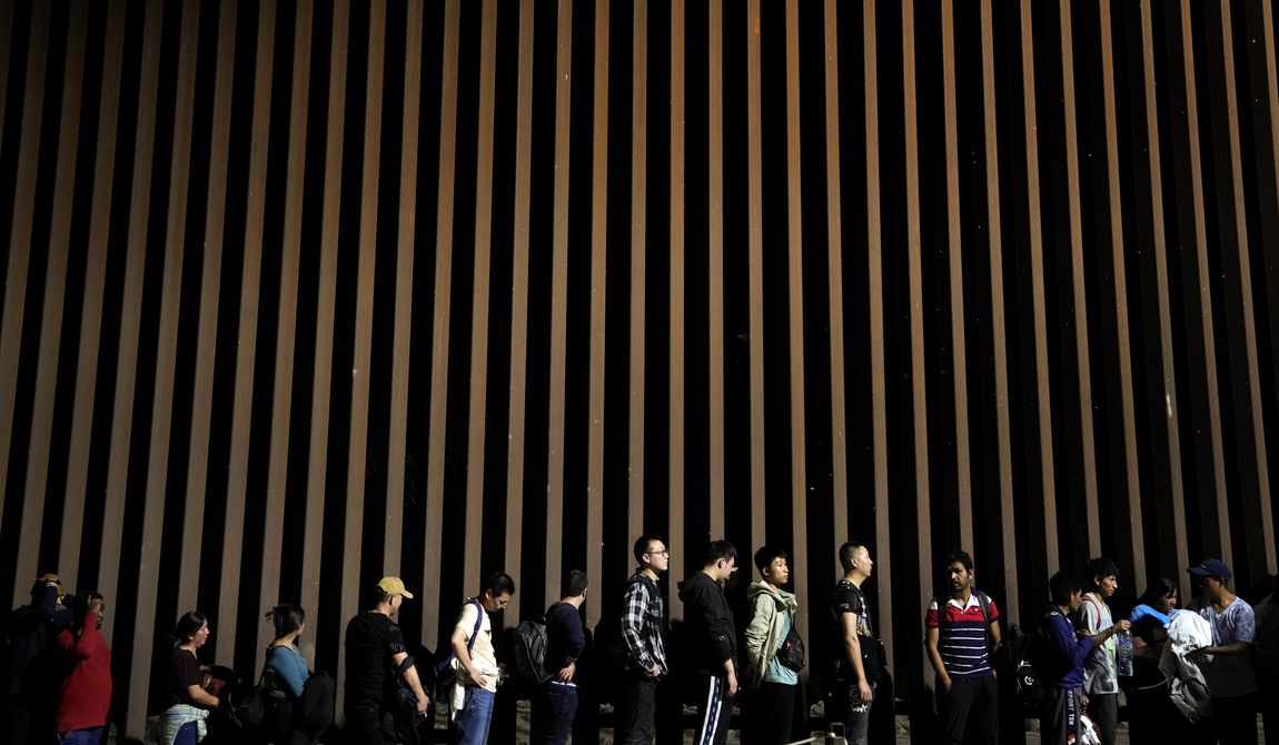 People line up against a border wall as they wait to apply for asylum after crossing the border from Mexico Tuesday, July 11, 2023, near Yuma, Ariz. (AP Photo/Gregory Bull)