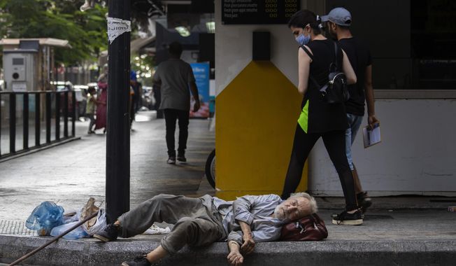 woman looks at a homeless Lebanese man sleeping on the ground in Hamra street, in Beirut, Lebanon, July 17, 2020. The World Bank has approved a $300 million additional financing to the poor in Lebanon in which families that live in poverty will get cash payments to help them through the country&#x27;s historic economic meltdown, the World Bank said in a statement released Friday, May 26, 2023. (AP Photo/Hassan Ammar, File)