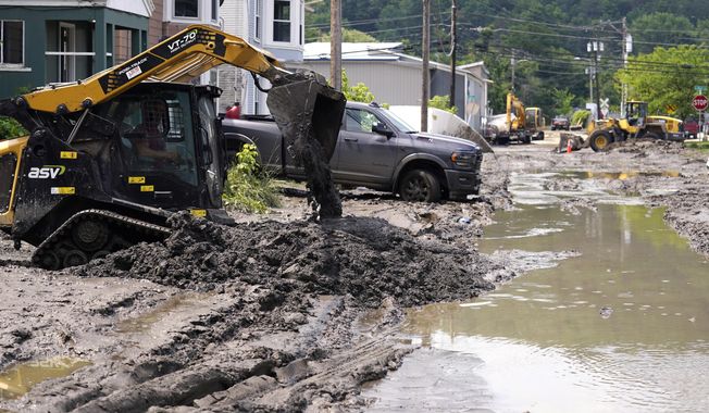 Equipment clears mud from a neighborhood as flood waters block a street, Wednesday, July 12, 2023, in Barre, Vt. Following a storm that dumped nearly two months of rain in two days, Vermonters are cleaning up from the deluge of water. (AP Photo/Charles Krupa)