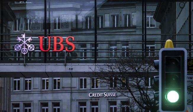 A traffic light signals green in front of the logos of the Swiss banks Credit Suisse and UBS in Zurich, Switzerland, March 19, 2023. UBS says it has completed its takeover of embattled rival Credit Suisse. The announcement comes nearly three months after the Swiss government hastily arranged a rescue deal to combine the country’s two largest banks. (Michael Buholzer/Keystone via AP, File)
